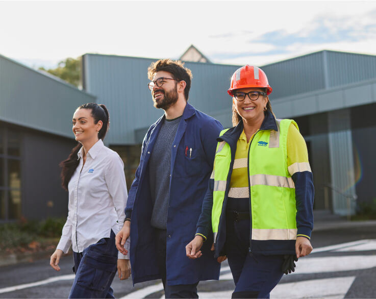 Three smiling BlueScope employees pose for a photo in front of a modern building